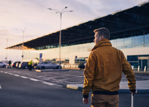 Young man with luggage walking to airport terminal at sunrise.