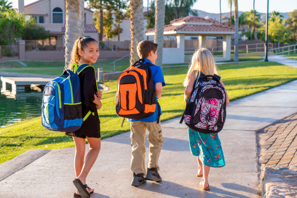 Students wearing backpacks, walk down path.
